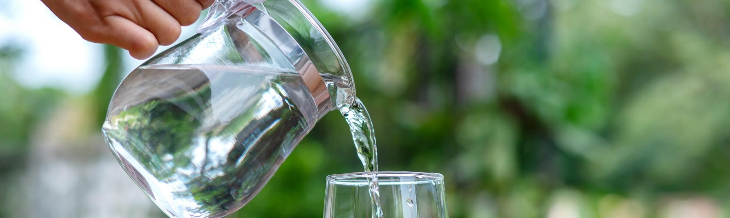 foto af glaskande der hælder vand i et glas ude i naturen