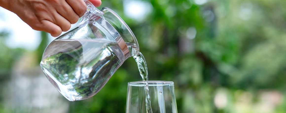 foto af glaskande der hælder vand i et glas ude i naturen