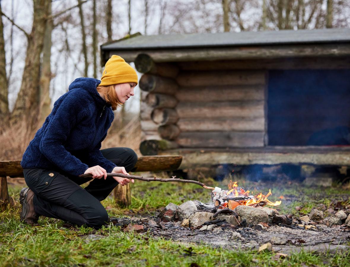 foto af kvinde der tænder bål foran shelter i skoven 