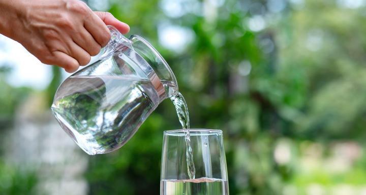 foto af glaskande der hælder vand i et glas ude i naturen